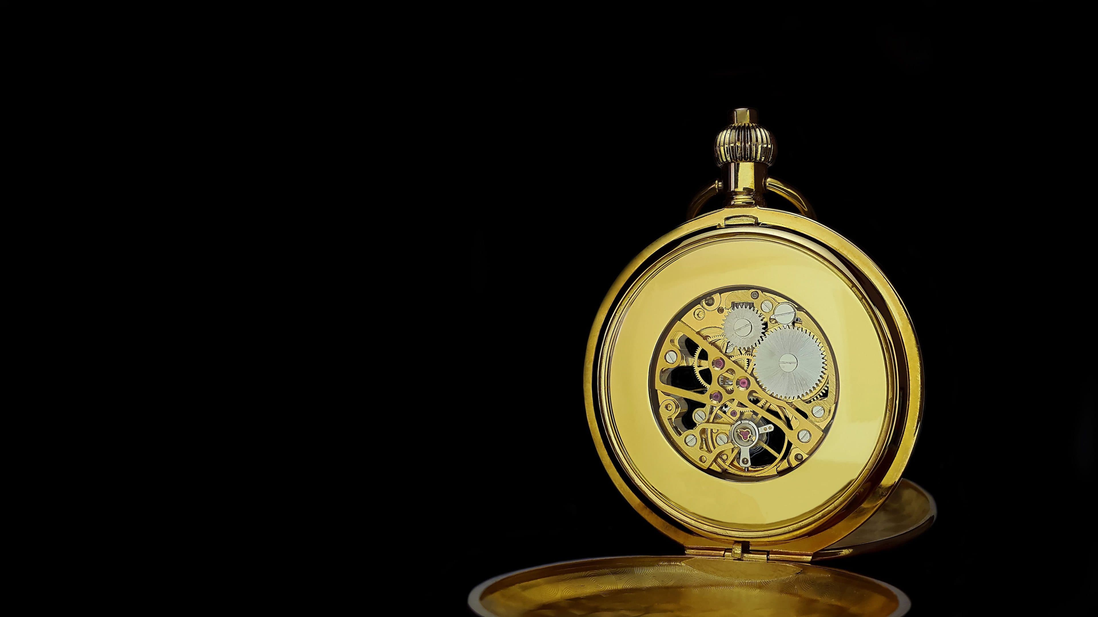 A gold watch open on black, its movement visible